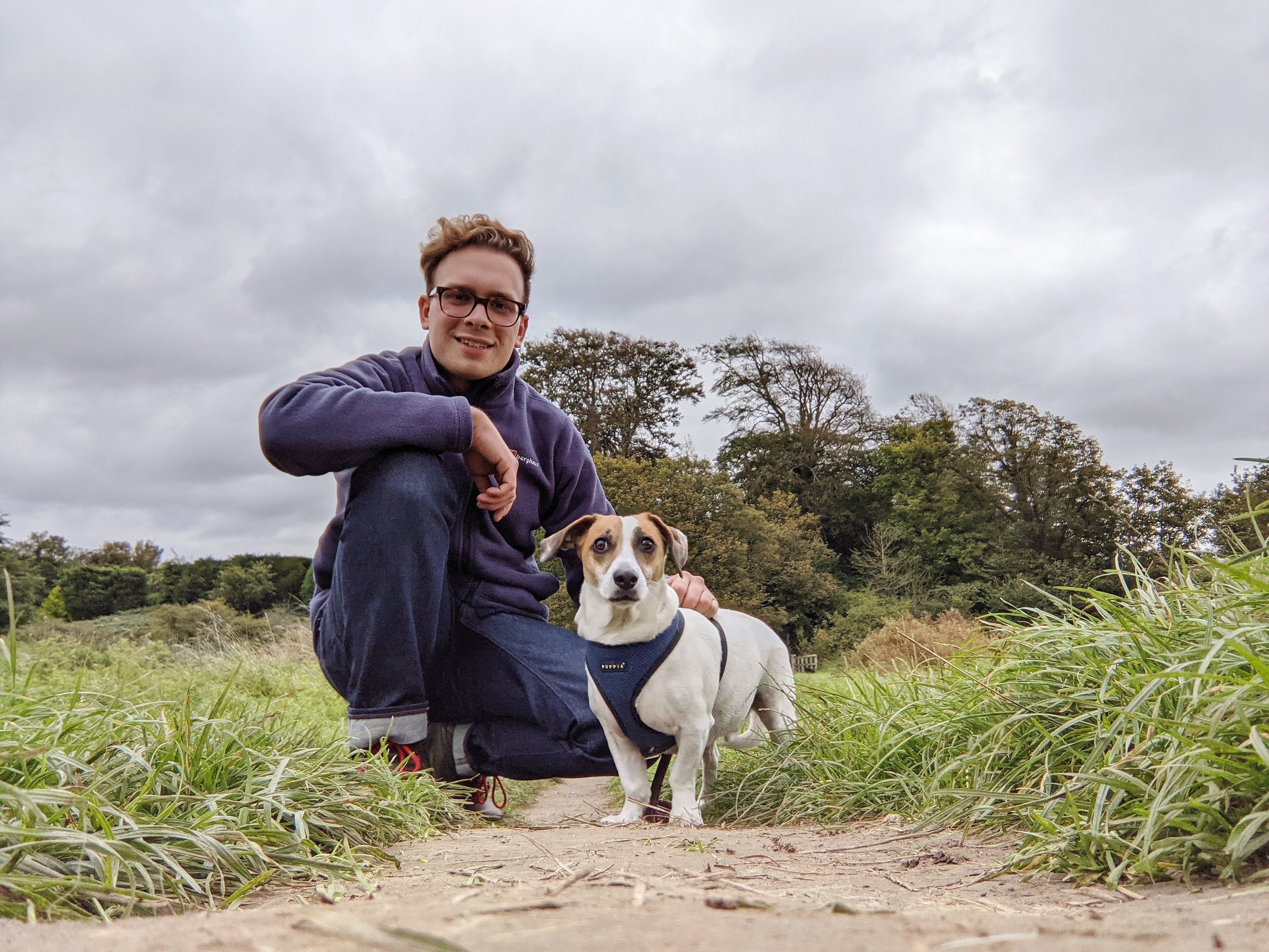 A photo of Dominic and Albie, his dog, on a walk with some woods behind them.